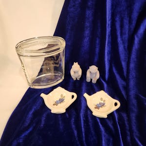 May include: Two small white ceramic teacup-shaped dishes with blue floral designs, two small white ceramic hippo figurines, and a clear glass jar with a lid.