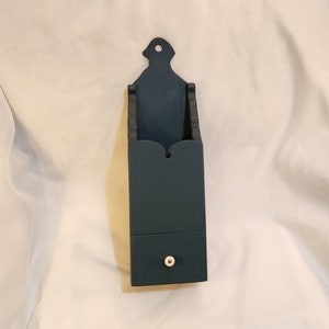 May include: A dark blue wooden wall mounted box with a small drawer. The drawer has a white knob.