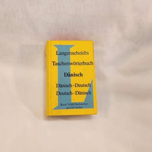 May include: A yellow and blue pocket dictionary with the title "Langenscheidts Taschenwörterbuch Dänisch" and the text "Dänisch-Deutsch Deutsch-Dänisch Rund 70000 Stichwörter auf 1105 Seiten".