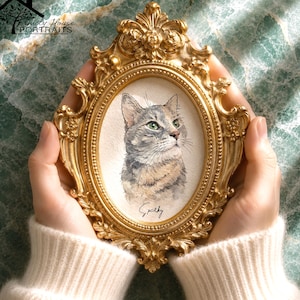 Puede incluir: Un marco de fotos ovalado de color dorado con detalles ornamentales de flores y volutas. Dentro del marco hay un retrato en acuarela de un gato atigrado gris con ojos verdes, que presenta el nombre Sparky escrito a mano bajo la imagen.