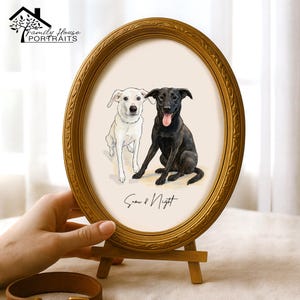 May include: An oval, gold-framed portrait featuring two dogs: a white dog and a black dog. The dogs are drawn in a watercolor style. The text "Snow & Night" is written below the dogs. The frame is displayed on a small wooden easel.