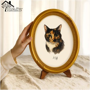 Könnte beinhalten: Ein ovaler, goldfarbener Bilderrahmen mit einer Aquarell-Illustration einer Glückskatze mit schwarzem, orangefarbenem und weißem Fell. Unter der Katze steht der Name Molly in schwarzer Schreibschrift. Der Rahmen steht auf einem kleinen Holzständer.