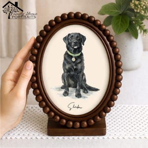May include: An oval-shaped picture frame with a dark brown wooden beaded border, containing a watercolor illustration of a black Labrador dog wearing a light green collar with a tag. The name Shadow is printed in black script below the dog.