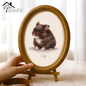Könnte beinhalten: Ein ovaler goldfarbener Rahmen mit einer verzierten, strukturierten Bordüre enthält eine Aquarellillustration eines braun-weißen Hamsters. Das Kunstwerk zeigt den Namen Molly in schwarzer Schreibschrift unter dem Hamster auf cremefarbenem Grund.