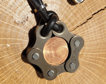 Peut inclure: Un pendentif en métal argenté en forme d'étoile avec une pièce de 1 euro au centre. Le pendentif est attaché à un cordon en cuir noir. Le pendentif porte les lettres "PVC" gravées sur le côté.