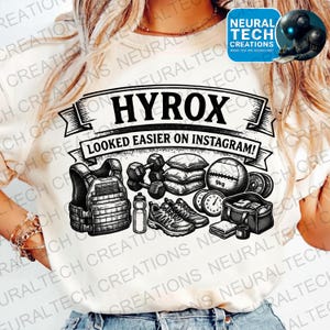May include: Cream-colored t-shirt with a graphic featuring the word "HYROX" above the phrase "LOOKED EASIER ON INSTAGRAM!" and illustrations of workout equipment, including a weight vest, dumbbells, and a medicine ball.