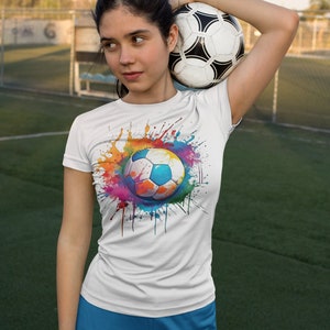 May include: A white t-shirt with a colorful paint splatter design featuring a soccer ball in the center. The soccer ball is white with black panels.