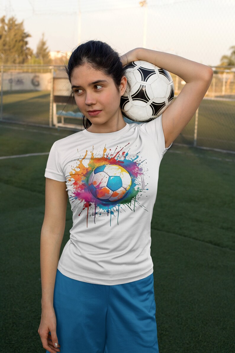 May include: A white t-shirt with a colorful paint splatter design featuring a soccer ball in the center. The soccer ball is white with black panels.