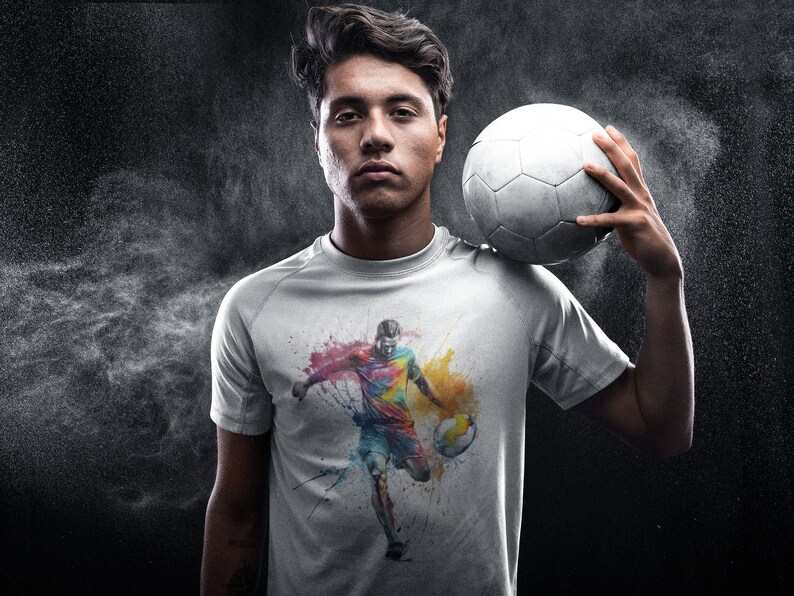 May include: A white t-shirt with a colorful graphic of a soccer player dribbling the ball. The graphic is painted in a watercolor style with splashes of color.