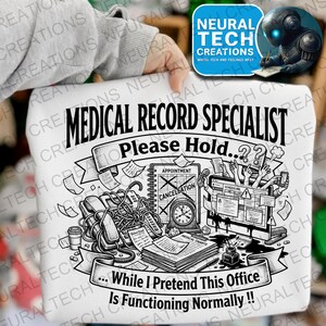 May include: A white sweatshirt featuring a black graphic print with the text MEDICAL RECORD SPECIALIST Please Hold... While I Pretend This Office Is Functioning Normally. The design includes a telephone, a clock, documents, and a computer screen.