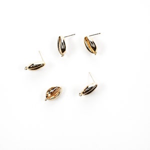May include: Four gold-colored shell-shaped earrings with posts. The earrings are arranged in a scattered pattern on a white background.