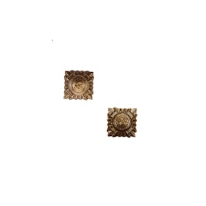 May include: Two antique brass square buttons with a detailed sunburst design. Each button features a central circular emblem surrounded by intricate patterns and a decorative border. The buttons are set against a white background.