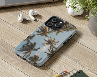 May include: A phone case with a tropical palm tree design. The case is white with a blue sky and green palm trees. The phone case has a camera lens cutout.