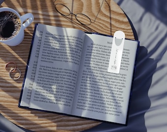 May include: An open book with a white bookmark that says "Life is an adventure" on a wooden table with a cup of coffee, two rings, and a pair of glasses. The book has text on the pages.