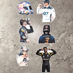 Peut inclure: Ensemble d'autocollants représentant des pilotes de Formule 1 et un casque de course. Le casque est orné d'un motif floral. Les pilotes sont en combinaisons de course, certains avec des casques, d'autres célébrant.