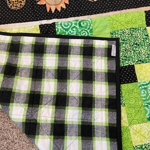 Puede incluir: Un edred&oacute;n hecho a mano con un patr&oacute;n de cuadros en blanco y negro en la parte inferior. La parte superior tiene un dise&ntilde;o de patchwork con telas verdes y blancas. El edred&oacute;n est&aacute; decorado con apliques con tem&aacute;tica de animales, incluyendo cabezas con forma de Mickey Mouse con estampados de leopardo, cebra y jirafa.