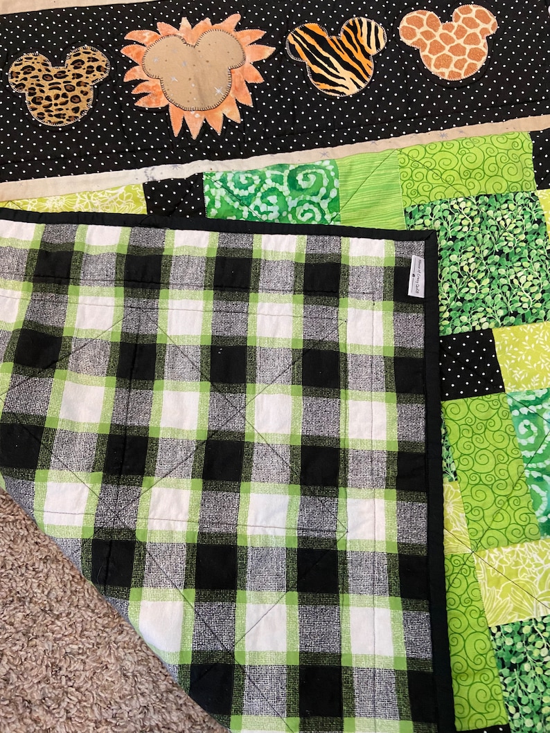Puede incluir: Un edred&oacute;n hecho a mano con un patr&oacute;n de cuadros en blanco y negro en la parte inferior. La parte superior tiene un dise&ntilde;o de patchwork con telas verdes y blancas. El edred&oacute;n est&aacute; decorado con apliques con tem&aacute;tica de animales, incluyendo cabezas con forma de Mickey Mouse con estampados de leopardo, cebra y jirafa.