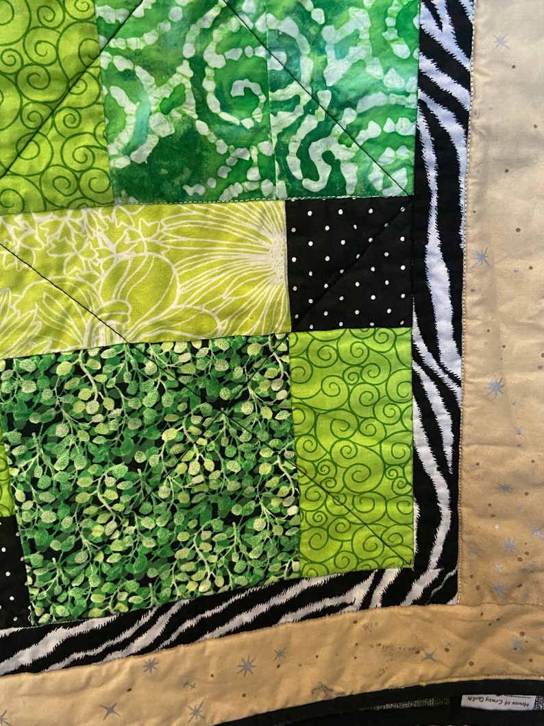Puede incluir: Un edred&oacute;n hecho a mano con un dise&ntilde;o de patchwork. El edred&oacute;n presenta cuadrados de tela verde con varios patrones, incluyendo espirales, estampados florales y lunares. Un borde con estampado de cebra enmarca el edred&oacute;n, con un reverso beige.