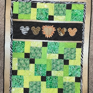 Puede incluir: Un edred&oacute;n hecho a mano con un tema de la jungla. El edred&oacute;n presenta un dise&ntilde;o de patchwork en tonos de verde, negro y blanco. El centro tiene dise&ntilde;os en forma de Mickey Mouse con estampados de animales. El borde es estampado de cebra.