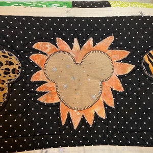 Puede incluir: Un edred&oacute;n hecho a mano con un dise&ntilde;o central en forma de Mickey Mouse con un patr&oacute;n de rayos de sol naranja. El edred&oacute;n tiene un fondo negro con lunares blancos y detalles de estampado de leopardo y cebra. El dise&ntilde;o est&aacute; cosido con hilo plateado.