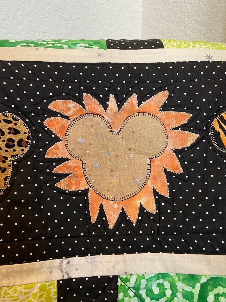 Puede incluir: Un edred&oacute;n hecho a mano con un dise&ntilde;o central en forma de Mickey Mouse con un patr&oacute;n de rayos de sol naranja. El edred&oacute;n tiene un fondo negro con lunares blancos y detalles de estampado de leopardo y cebra. El dise&ntilde;o est&aacute; cosido con hilo plateado.