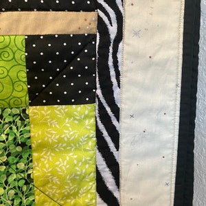 Puede incluir: Primer plano de un edred&oacute;n con dise&ntilde;o de patchwork. El edred&oacute;n presenta cuadrados negros con lunares blancos, verdes con patrones de hojas blancas y un borde de estampado de cebra. Los bordes son negros.