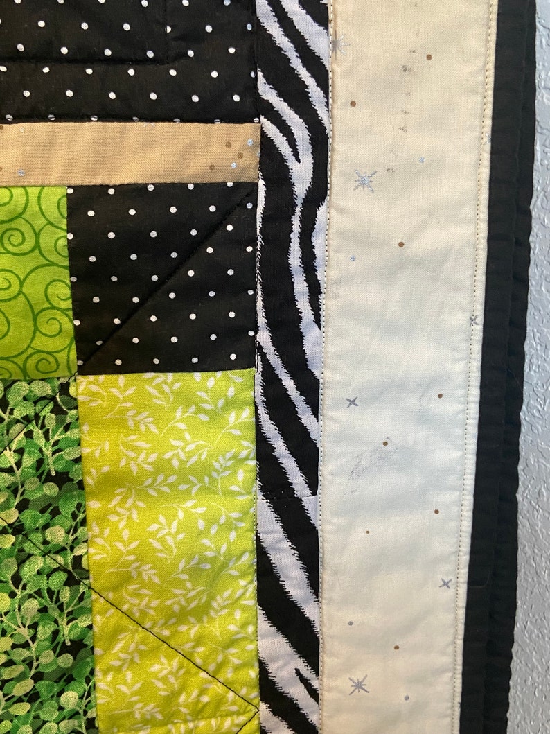 Puede incluir: Primer plano de un edred&oacute;n con dise&ntilde;o de patchwork. El edred&oacute;n presenta cuadrados negros con lunares blancos, verdes con patrones de hojas blancas y un borde de estampado de cebra. Los bordes son negros.