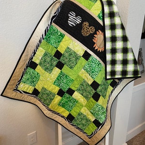 Puede incluir: Un edred&oacute;n hecho a mano con un dise&ntilde;o de patchwork. El edred&oacute;n presenta cuadrados de telas verdes, negras y blancas con varios patrones. Los acentos incluyen estampado de cebra, un coraz&oacute;n en blanco y negro y un coraz&oacute;n con estampado de leopardo. El edred&oacute;n est&aacute; bordeado con un borde negro.