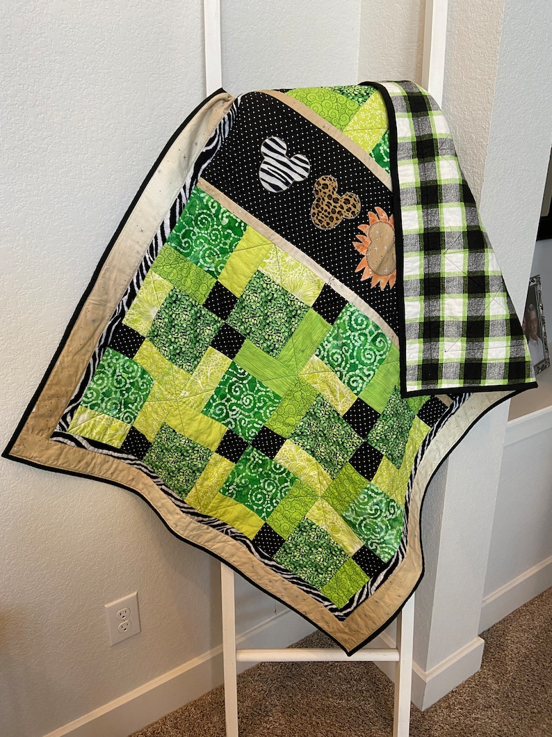 Puede incluir: Un edred&oacute;n hecho a mano con un dise&ntilde;o de patchwork. El edred&oacute;n presenta cuadrados de telas verdes, negras y blancas con varios patrones. Los acentos incluyen estampado de cebra, un coraz&oacute;n en blanco y negro y un coraz&oacute;n con estampado de leopardo. El edred&oacute;n est&aacute; bordeado con un borde negro.