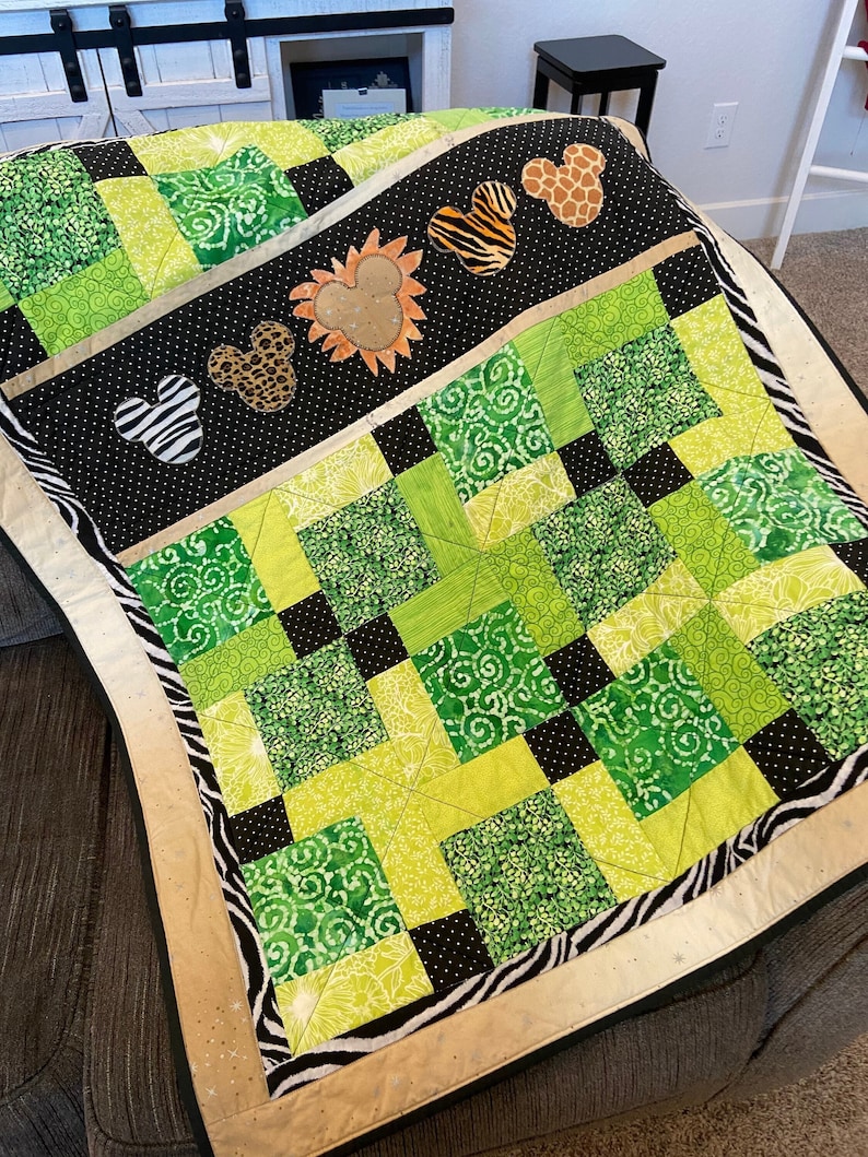 Puede incluir: Un edred&oacute;n hecho a mano con un dise&ntilde;o de patchwork en tonos verdes y negros. El edred&oacute;n tiene un borde negro con lunares blancos y formas de Mickey Mouse con estampado animal. Los bordes est&aacute;n ribeteados con tela de estampado de cebra.