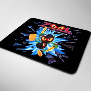 Könnte beinhalten: Schwarze Mauspad mit einer blauen und weißen Grafik eines Comic-Charakters namens Zool, der ein Schwert hält und vor einem zerbrochenen Glaseffekt steht. Der Text "Zool" und "Into the 5th Dimension" ist in Weiß geschrieben.