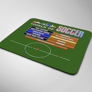 Puede incluir: Alfombrilla de ratón verde con un campo de fútbol pixelado y el texto "Sensible World of Soccer" en un esquema de colores arcoíris. Las opciones del menú incluyen "Edit Tactics", "Edit Custom Teams", "Highlights", "Options", "Save Disk Filing", "Load Old Competition", "Friendly", "DIY Competition", "Preset Competition", "Season" y "Career".