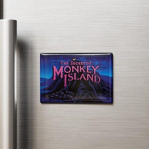 Może przedstawiać: Prostokątny magnes z napisem "The Secret of Monkey Island" w kolorze różowym i białym na tle ciemnoniebieskiej i fioletowej scenerii górskiej. Magnes jest przymocowany do srebrnej lodówki.