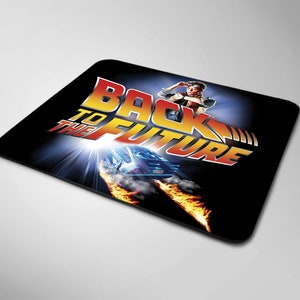 May include: Black mouse pad with a graphic of the DeLorean time machine from the movie Back to the Future. The text "Back to the Future" is in a stylized font with a red, yellow, and blue color scheme.