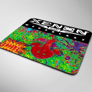 Peut inclure: Un tapis de souris noir avec un motif pixelisé coloré représentant une créature rouge et le texte "XENON MEGABLAST" en blanc.