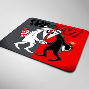 May include: A square mousepad featuring the Spy vs. Spy characters shaking hands. One character is in a white suit, holding dynamite, and the other is in a black suit, holding a lit bomb. The background is split, with gray and red sections, and the words "SPY vs SPY" are at the top.
