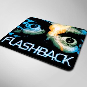 May include: A rectangular mouse pad featuring a dark background with two large, detailed human eyes staring forward. The word FLASHBACK is printed in large, metallic, blue-tinted capital letters across the bottom portion of the design.