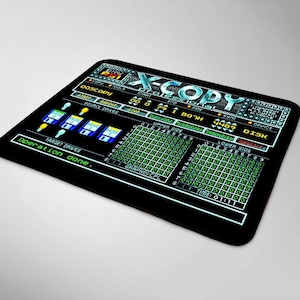 Puede incluir: Una alfombrilla de ratón negra con un gráfico verde y azul de una pantalla de ordenador que muestra el texto "X-COPY PROFESSIONAL" y una interfaz de programa con el texto "DOSCOPY" y "Operación completada."
