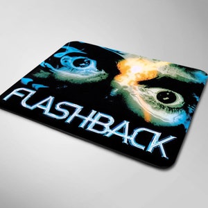 Op de afbeelding: Een zwarte muismat met een blauwe en groene afbeelding van een oog en het woord "FLASHBACK" in een blauw en wit lettertype.