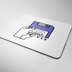 May include: A purple floppy disk with the text "AMIGA Work Bench V1.3" on it. A hand is holding the floppy disk.