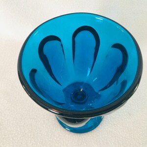 May include: A blue glass bowl with a scalloped rim and black lines. The bowl has a pedestal base.