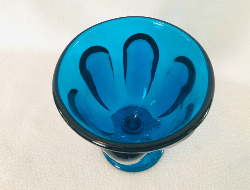 May include: A blue glass bowl with a scalloped rim and black lines. The bowl has a pedestal base.