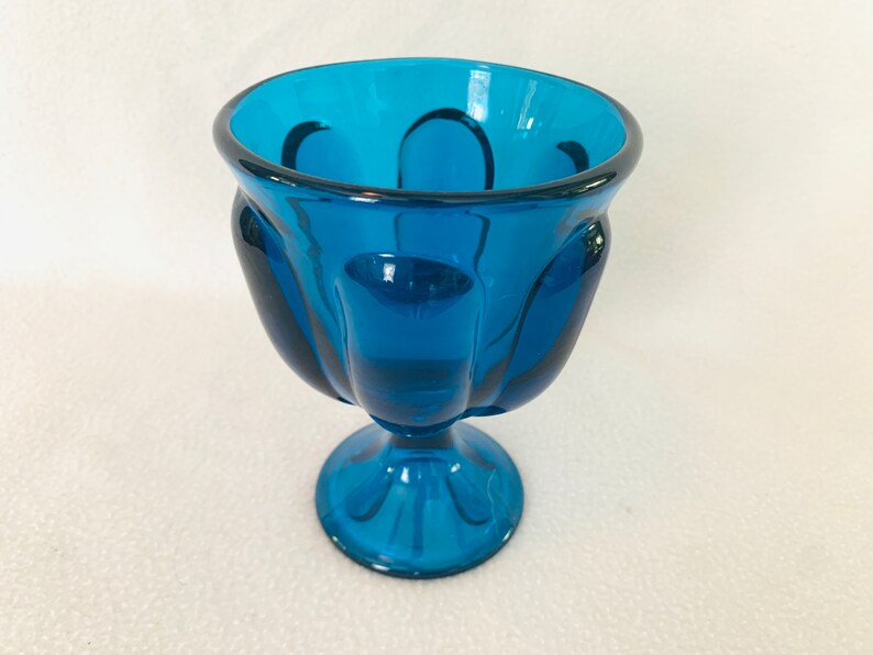 May include: A teal blue glass bowl with a fluted design and a pedestal base.