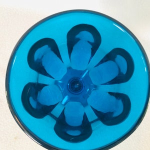 May include: A blue glass drinking glass with a flower-shaped design on the bottom.