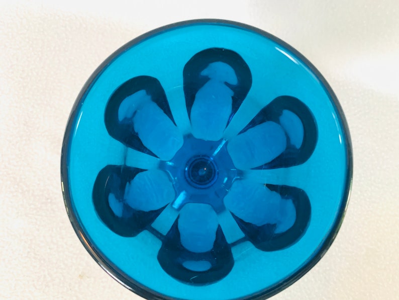 May include: A blue glass drinking glass with a flower-shaped design on the bottom.