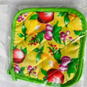 May include: A yellow quilted pot holder with a green border. The pot holder has a pattern of red apples, green leaves, and purple flowers.