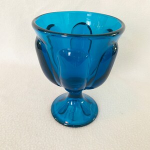 May include: A teal blue glass bowl with a fluted design and a pedestal base.