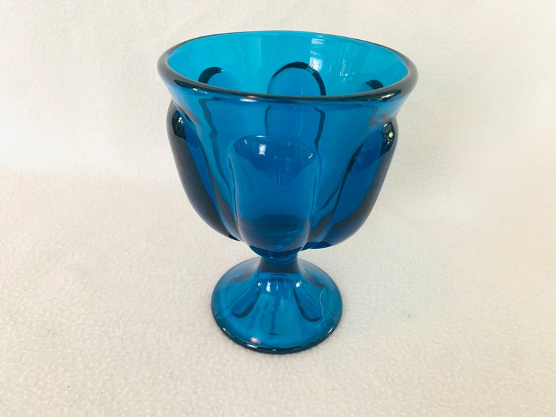 May include: A teal blue glass bowl with a fluted design and a pedestal base.