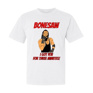 Puede incluir: Camiseta blanca con una ilustración roja y negra de un luchador con el texto "Bonesaw I got you for three minutes!"