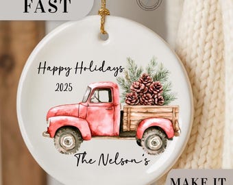 May include: A white ceramic holiday ornament featuring a red vintage truck carrying pine cones and greenery. The ornament has the text "Happy Holidays 2025" and "The Nelson's". A gold string is attached for hanging.
